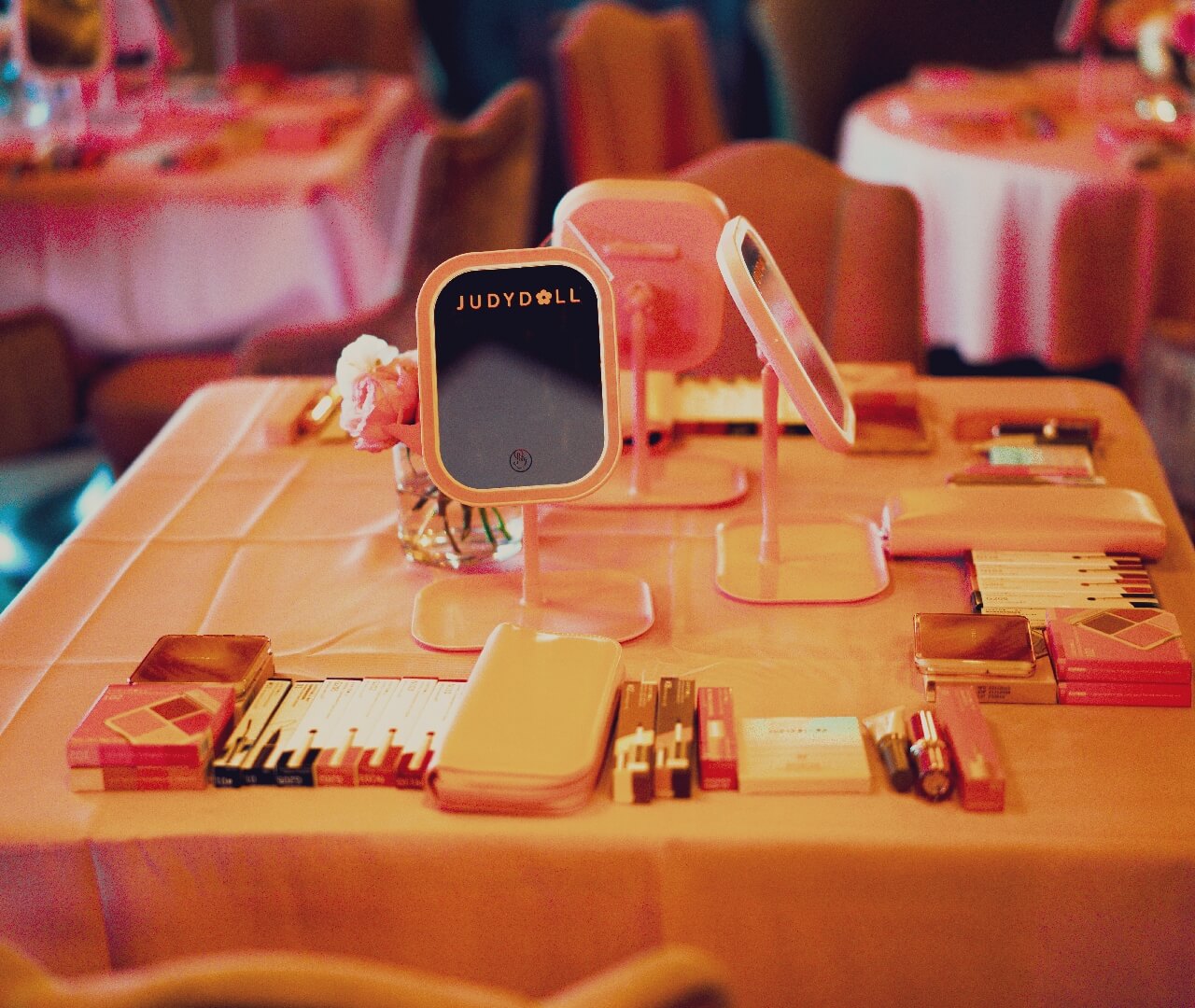 Corporate Event Product Launch Tabletop Display Elegant brand activation tabletop setup featuring custom illuminated vanity mirrors, neatly arranged cosmetic products, and premium pink table linens for a high-end corporate product launch and experiential marketing event production.