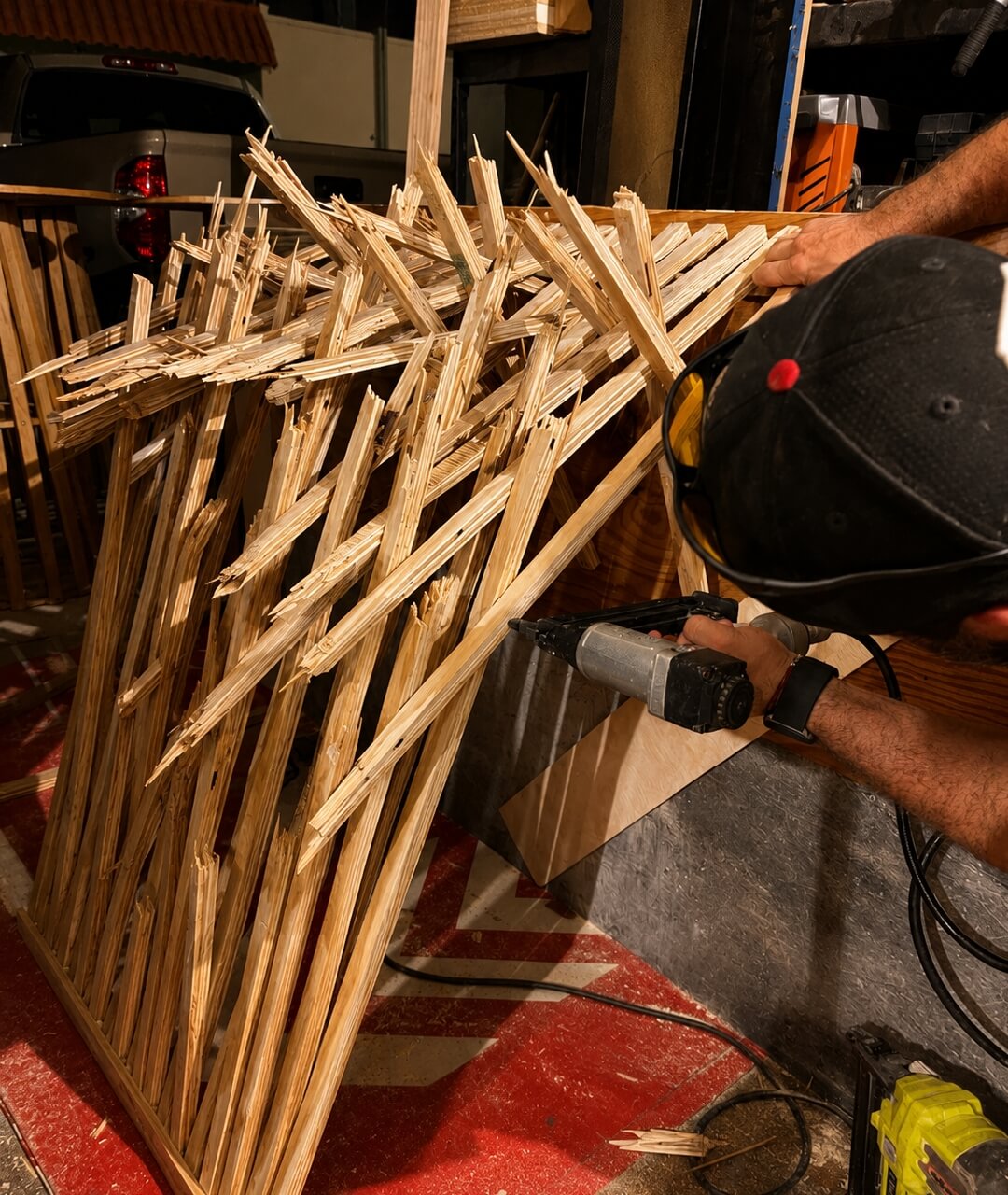 Custom Stage Scenery And DJ Booth Fabrication Technician using a nail gun to assemble a custom textured wooden facade for an event stage or DJ booth, showcasing creative event production and design rental services.