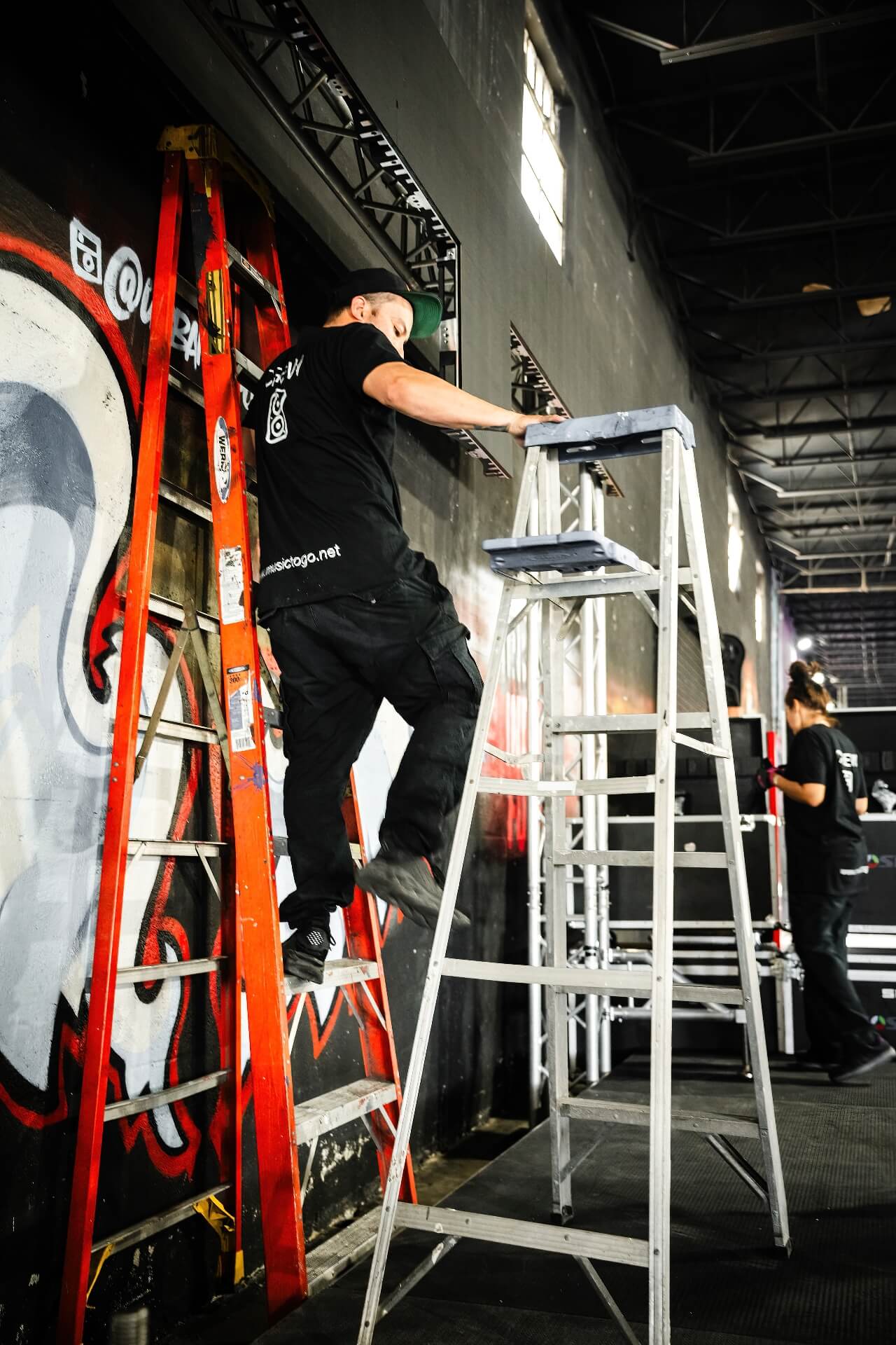 Indoor Event Stage Production Truss Installation Professional audio and lighting crew using ladders to install stage equipment truss systems for an indoor concert, DJ performance, or commercial event production rental setup.
