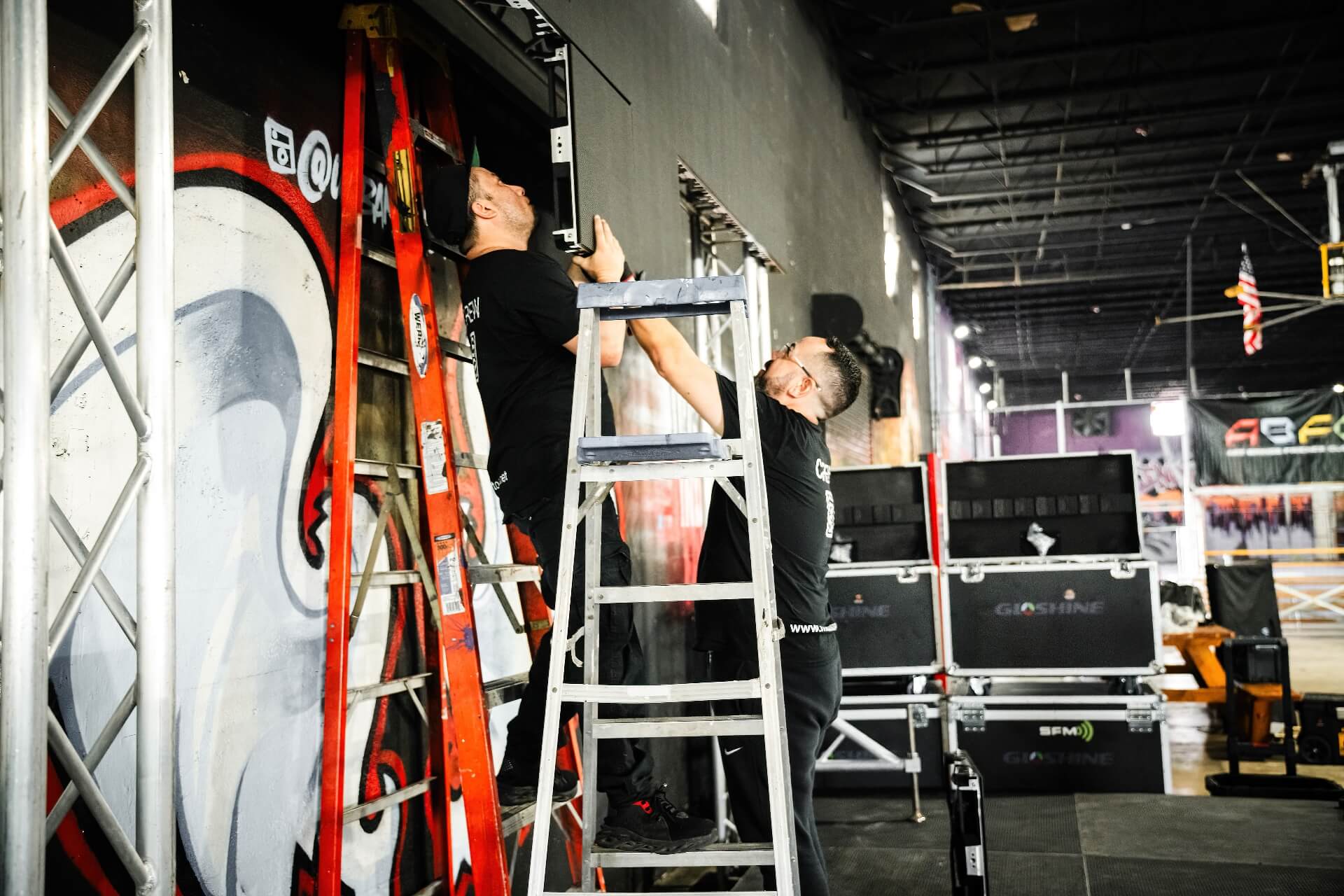 Indoor Stage LED Screen Panel Production Setup Event production crew installing professional LED video wall panel components on an indoor stage truss structure, complete with flight cases for premium audio and lighting rentals.