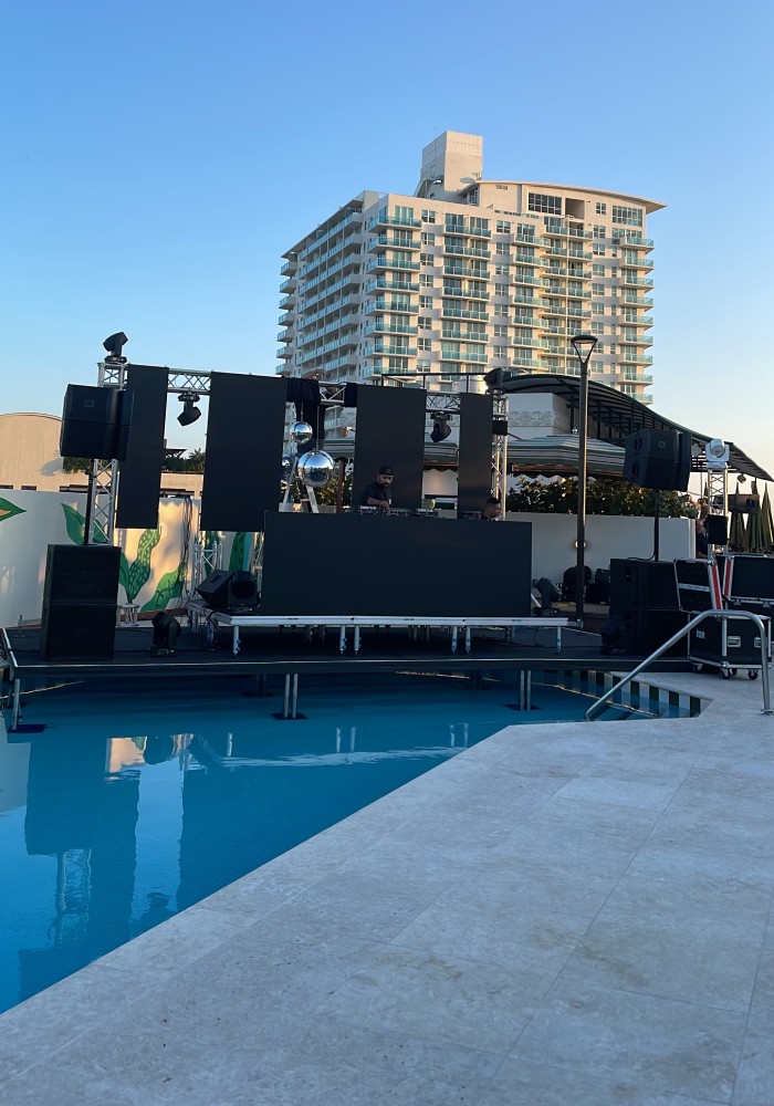 Poolside DJ Booth Production Music To Go premium outdoor DJ booth setup featuring large LED screens, professional sound system speakers, and lighting equipment for a luxury poolside event.