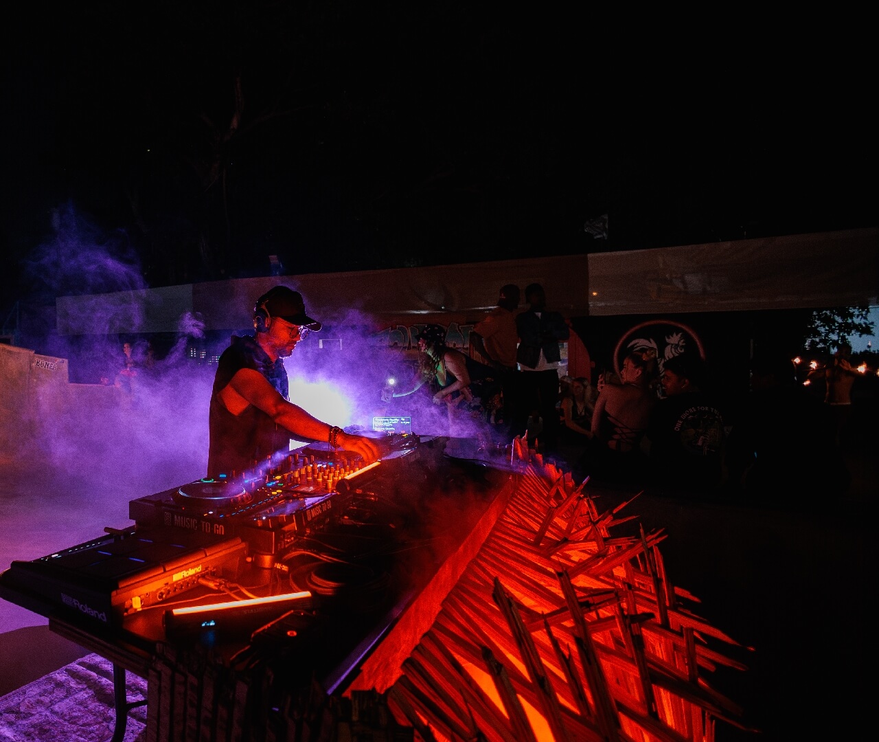 Professional DJ Audio Equipment Event Production Setup Live DJ performing at night with professional audio equipment, a custom illuminated wood booth, atmospheric smoke machine effects, and stage lighting for a premium event production rental experience.